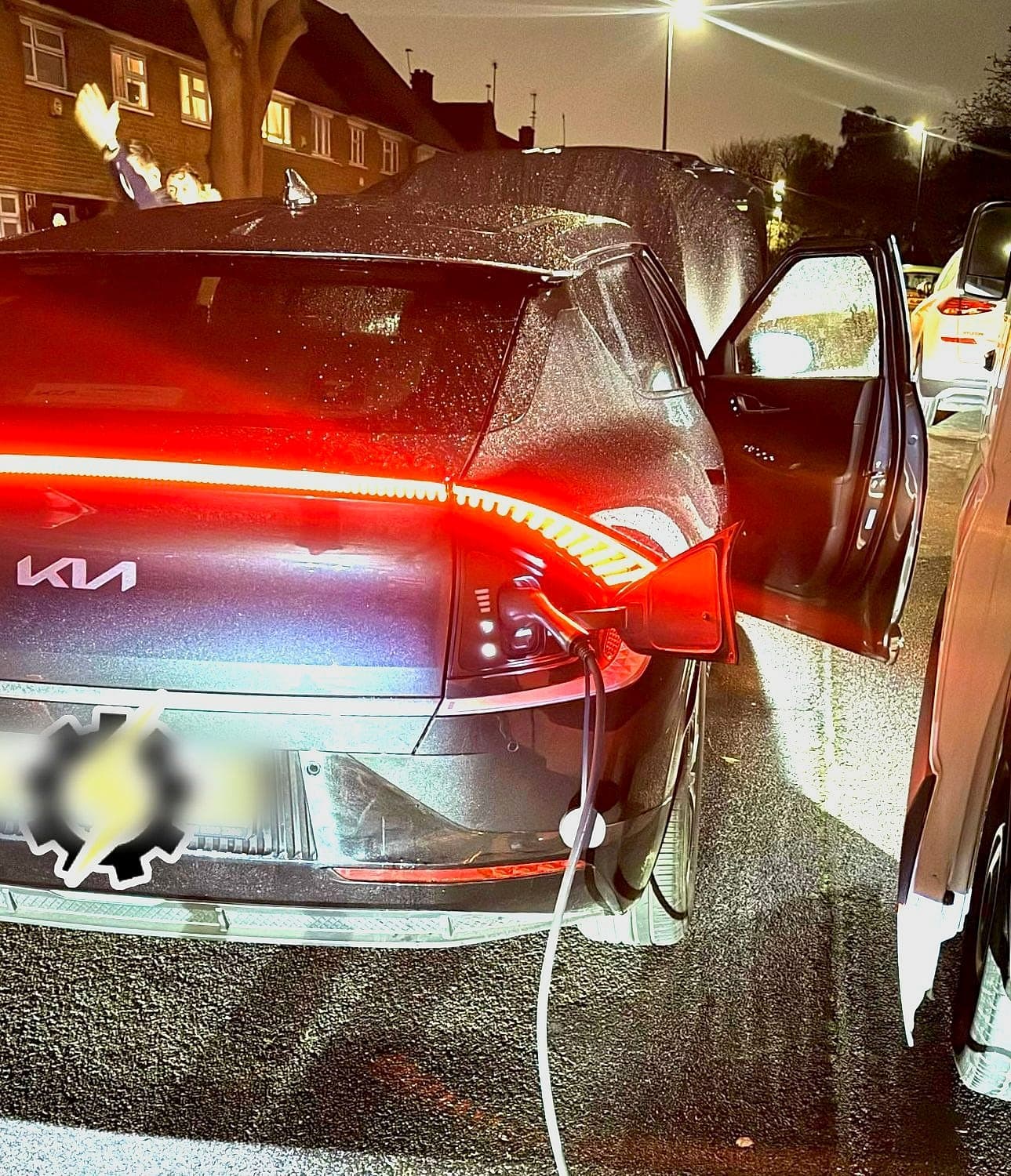 A Kia EV6 on charge at night, its rear light bar glowing