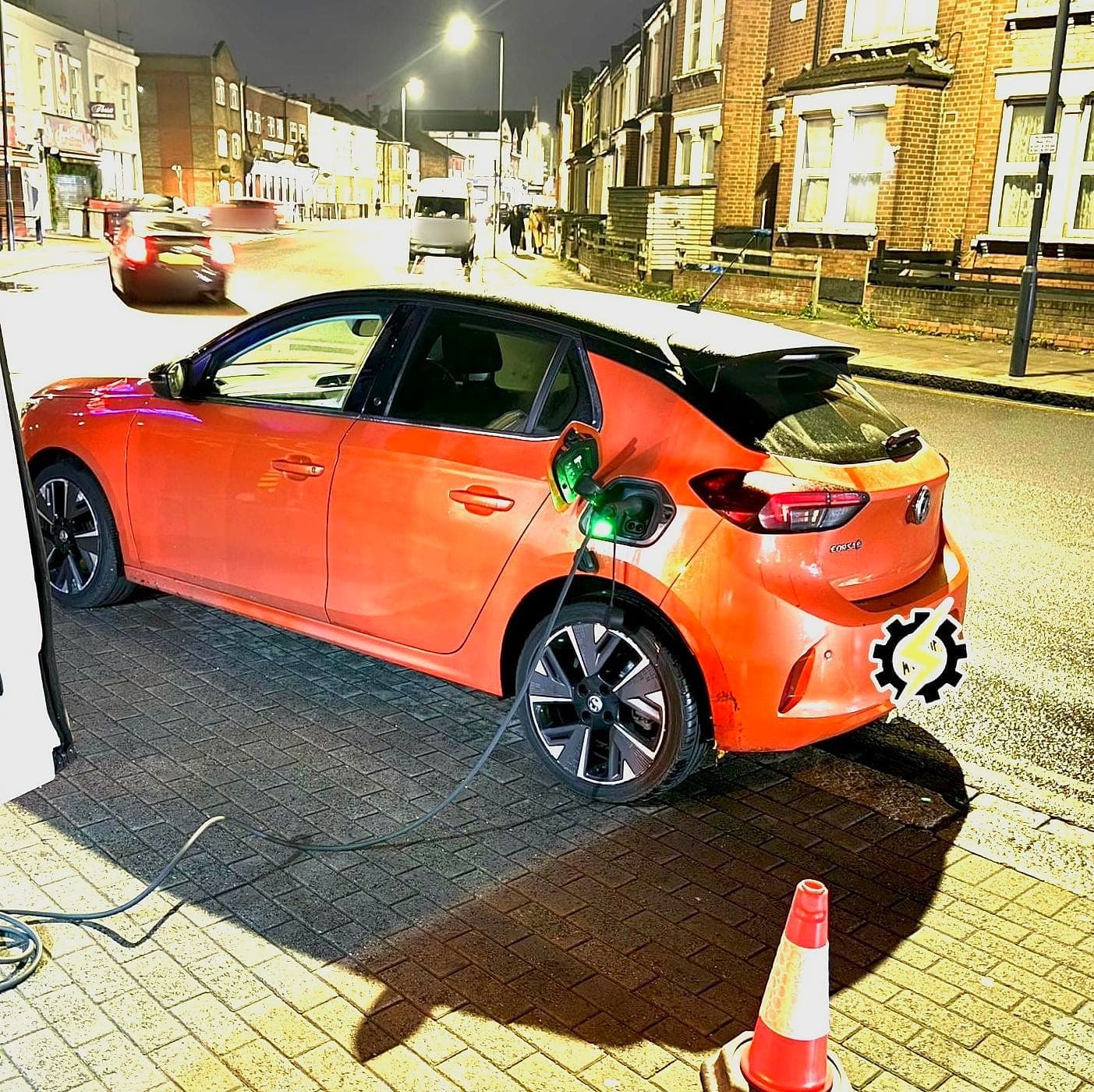 An orange Vauxhall Corsa Electric on charge at the kerb on a lit street at night