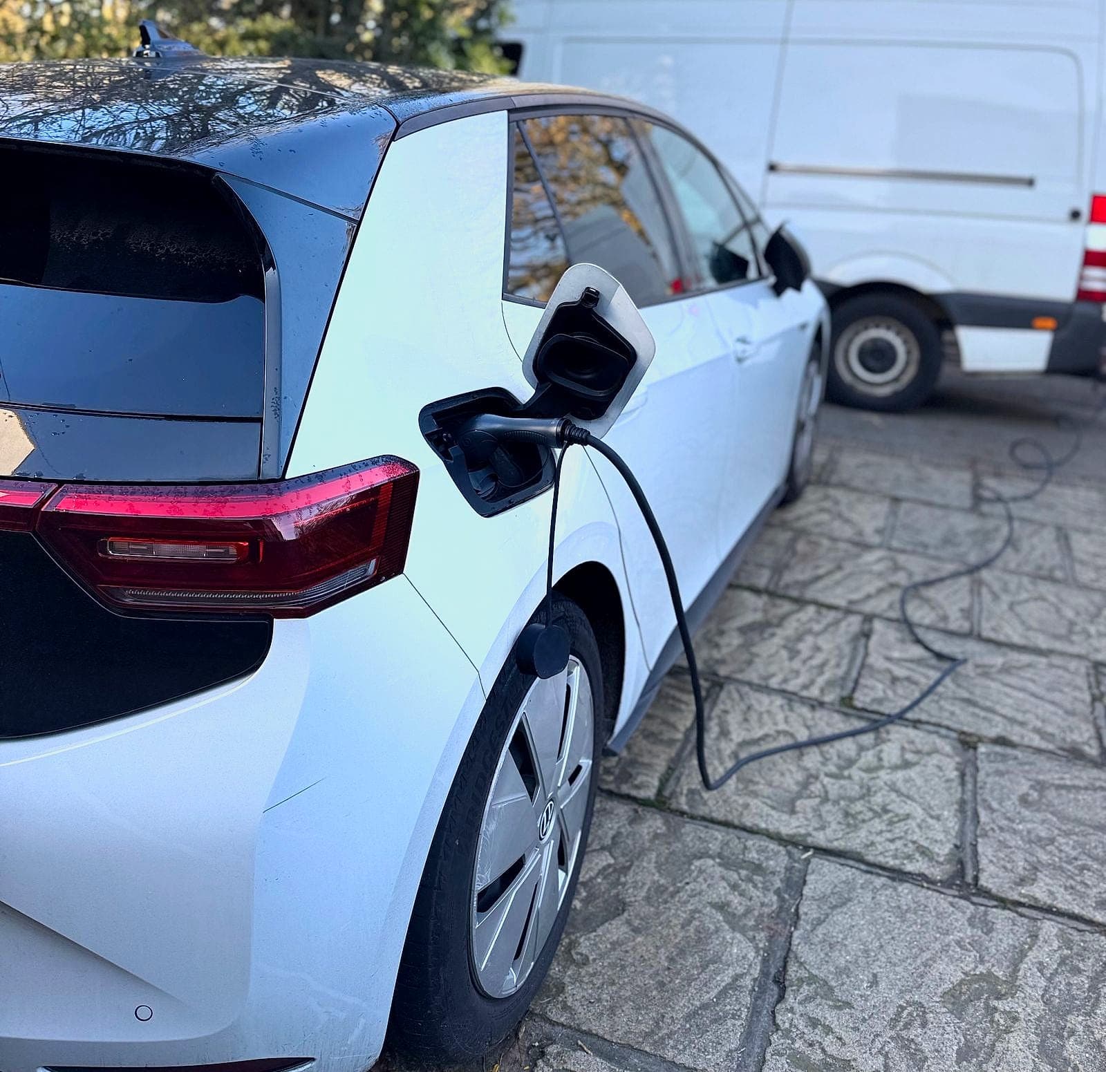 A white Volkswagen ID.3 with the charge cable plugged in, in a paved courtyard
